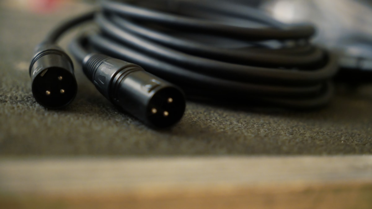 Dois conectores XLR macho de cabo de microfone em close, com cabo enrolado ao fundo